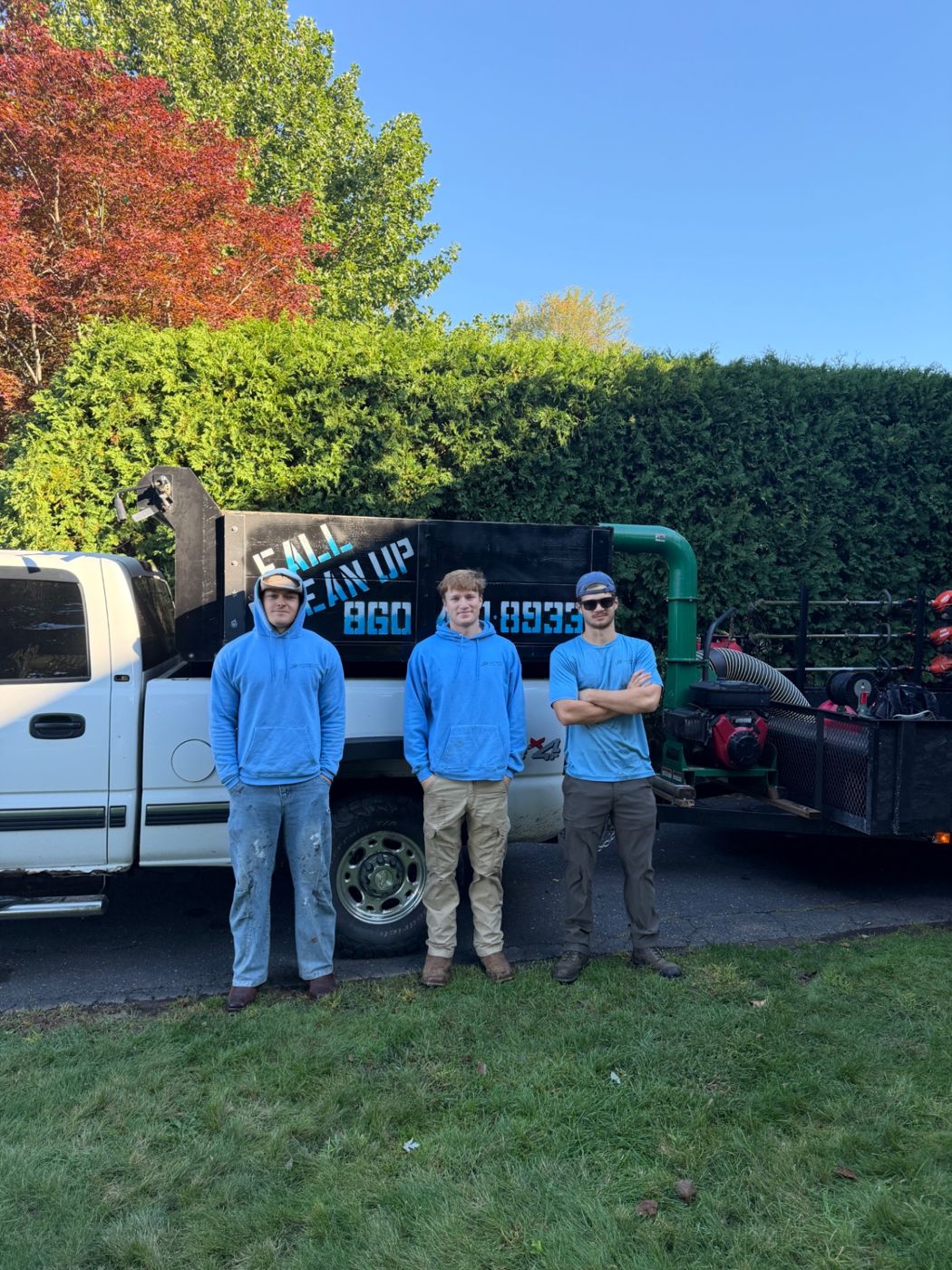 Three crew members in blue standing in front of a white work truck and leaf cleanup equipment